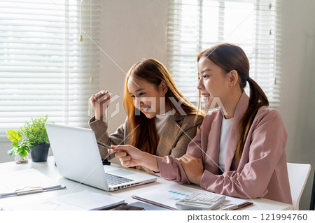 Businesswoman sitting at desk on couch in workplace or at home working on laptop and analyzing data on charts and graphs and writing on papers to make business plan and strategies for company Businesswoman sitting at desk on couch in workplace or at home working on laptop and analyzing data on charts and graphs and writing on papers to make business plan and strategies for company 121994760