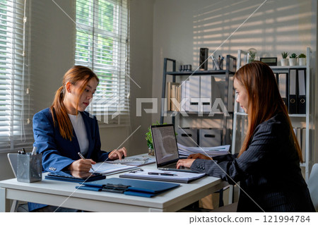 Businesswoman sitting at desk on couch in workplace or at home working on laptop and analyzing data on charts and graphs and writing on papers to make business plan and strategies for company Businesswoman sitting at desk on couch in workplace or at home working on laptop and analyzing data on charts and graphs and writing on papers to make business plan and strategies for company 121994784