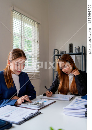 Businesswoman sitting at desk on couch in workplace or at home working on laptop and analyzing data on charts and graphs and writing on papers to make business plan and strategies for company 121994792