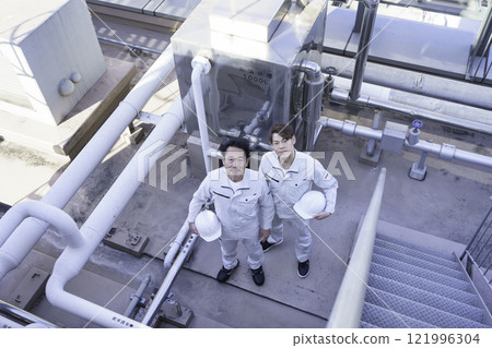 Two men in work clothes standing in front of the water supply and drainage equipment on the roof. Photo courtesy of Tokyo Electronics College, Denpa Gakuen Corporation. Two men in work clothes standing in front of the water supply and drainage equipment on the roof. Photo courtesy of Tokyo Electronics College, Denpa Gakuen Corporation. 121996304
