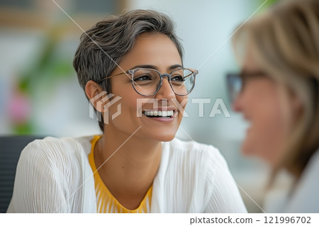 Woman smiling during conversation in bright office setting with another person 121996702