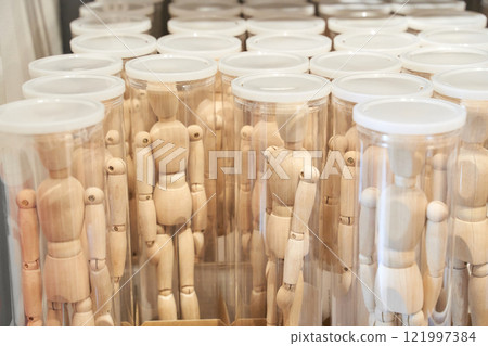 Wooden art mannequins standing in transparent cylindrical containers Wooden art mannequins standing in transparent cylindrical containers 121997384