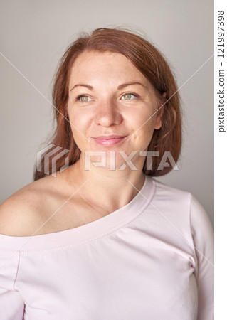 Caucasian female adult with red hair and green eyes smiling in light pink top 121997398