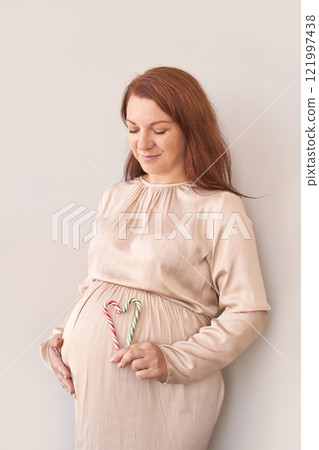 Caucasian pregnant female holding candy canes over belly with gentle smile 121997438