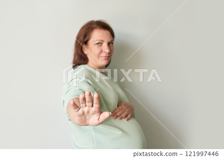 Pregnant caucasian adult female gesturing stop with hand in minimalist setting Pregnant caucasian adult female gesturing stop with hand in minimalist setting 121997446