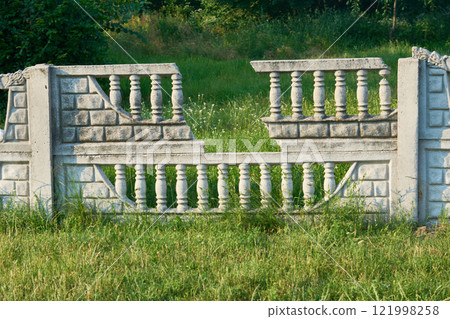An ancient ruined stone fence with carved balustrade decorations 121998258