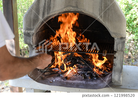 Hand keeps fire going in a grill with fiery flames - an empty fire grate 121998520