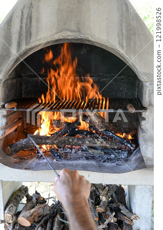 Hand keeps fire going in a grill with fiery flames - an empty fire grate 121998526