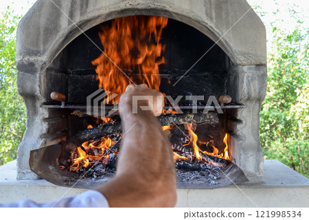Hand keeps fire going in a grill with fiery flames - an empty fire grate 121998534