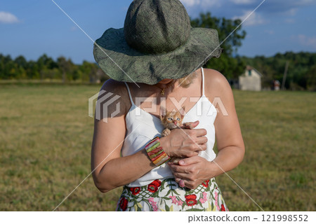Woman with a summer hat holding a small yellow kitten in the countryside, in summertime 121998552