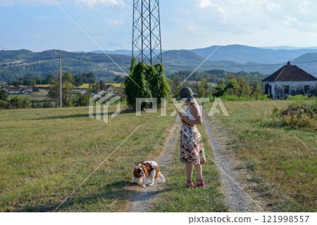 Woman with a dog holds a little yellow kitten on a country road, in summer Woman with a dog holds a little yellow kitten on a country road, in summer 121998557