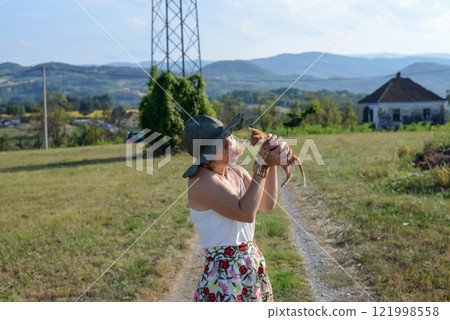 Woman with a hat is holding a small yellow kitten in the countryside, in summertime - exclusively reserved for real pet lovers Woman with a hat is holding a small yellow kitten in the countryside, in summertime - exclusively reserved for real pet lovers 121998558