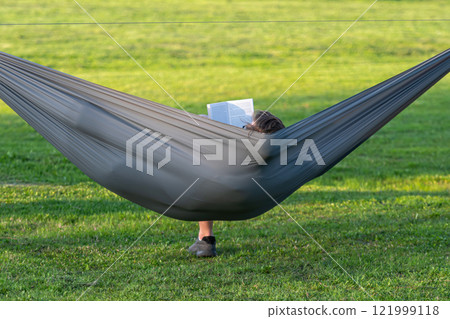 man reading book in comfortable hammock at green garden, viev from behind man reading book in comfortable hammock at green garden, viev from behind 121999118