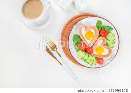 Breakfast on Valentine's Day fried eggs sausages in the shape of a heart and cup of coffee on a white background top view. copy space Breakfast on Valentine's Day fried eggs sausages in the shape of a heart and cup of coffee on a white background top view. copy space 121999138