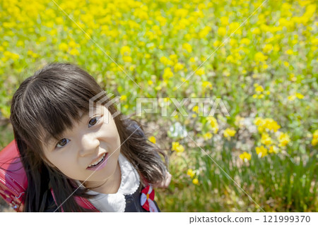 一名一年級學生背著書包走過油菜花盛開的公園 121999370