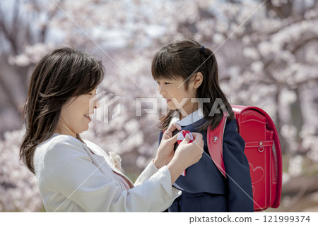 在櫻花公園裡，一位母親為背著書包的女兒繫上絲帶 121999374