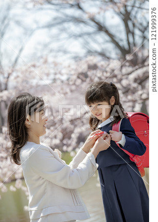 在櫻花公園裡，一位母親為背著書包的女兒繫上絲帶 121999376