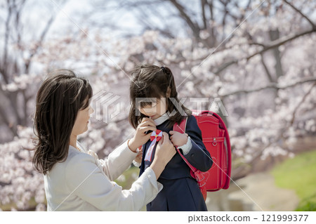 在櫻花公園裡，一位母親為背著書包的女兒繫上絲帶 121999377