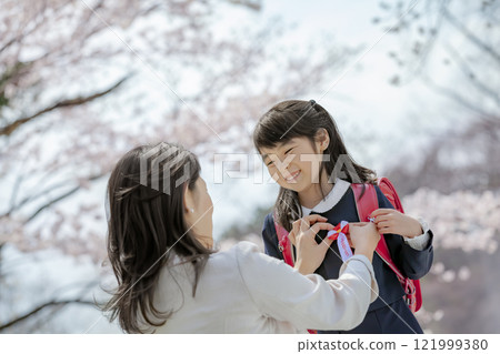 在櫻花公園裡,一位母親為背著書包的女兒繫上絲帶 在櫻花公園裡,一位母親為背著書包的女兒繫上絲帶 121999380