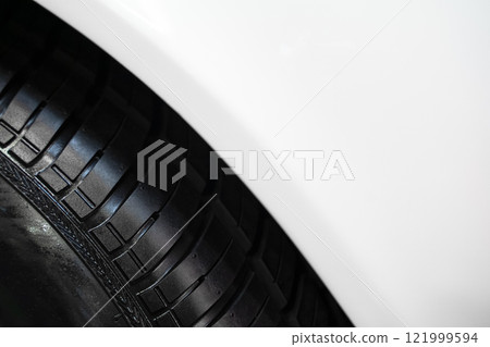 detail of car wheel black rubber tire on the front wing fender of white car 121999594
