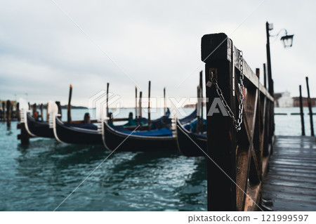 Wooden pier leading to gondolas in calm water 121999597