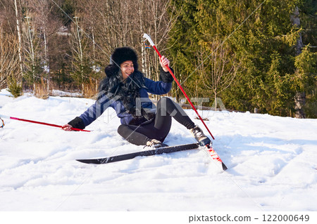 Laughing cheerful young girl fell down while skiing in the forest 122000649
