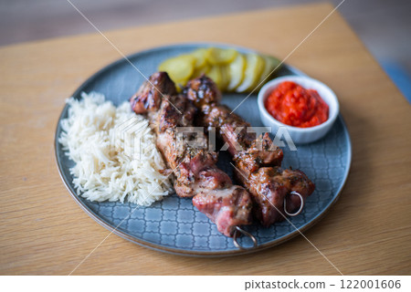 Grilled meat BBQ with rices, cucumber, salads and sauce served on stylish plate on wooden table 122001606