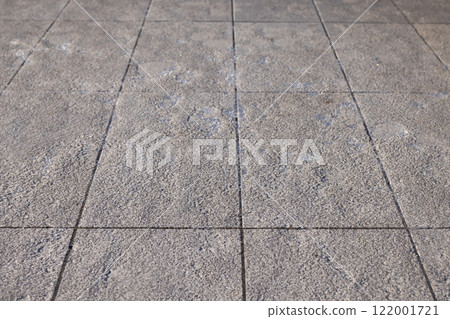 A close-up of grey paving stones showing patches of ice and frost, highlighting the slippery surface and subtle signs of winter conditions. 122001721