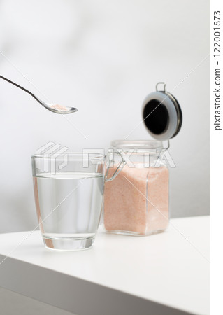 A spoon of Himalayan salt is being added to a glass of drinking water 122001873