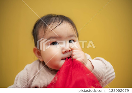 A baby with teary eyes sitting on a yellow background 122002079