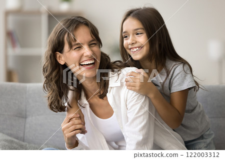 Cheerful young Hispanic mother piggybacking her adorable daughter 122003312