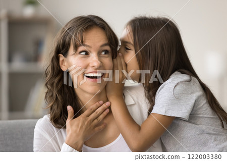 Close up of little daughter sharing secret in moms ear 122003380