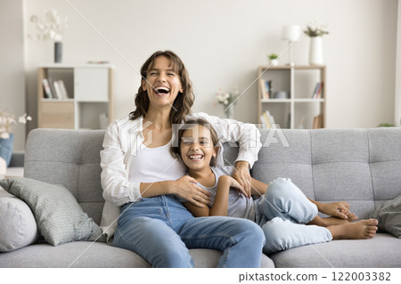 Happy young woman hugging her small adorable daughter seated indoors 122003382