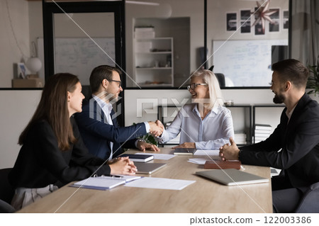 Two business partners shaking hands seated around office table Two business partners shaking hands seated around office table 122003386