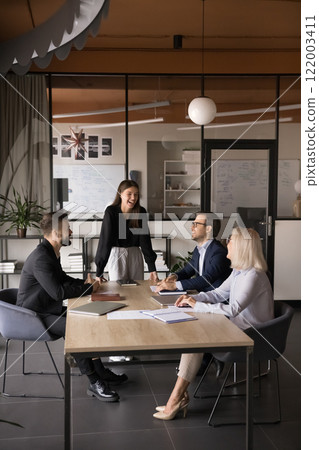 Businesspeople laughing, joking seated around table during presentation 122003411