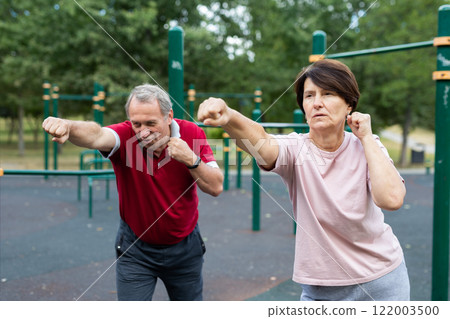 Elderly man and woman doing gymnastics on outdoor sports ground 122003500