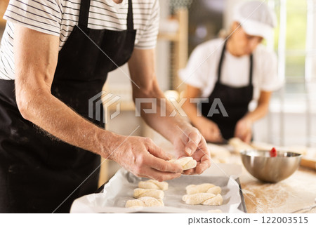 Baker's hands fold pieces of dough on baking sheet Baker's hands fold pieces of dough on baking sheet 122003515