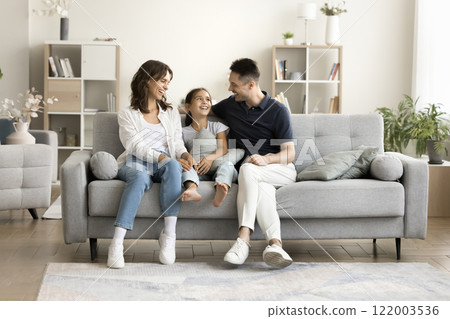 Little girl talking with parents seated on sofa at home Little girl talking with parents seated on sofa at home 122003536