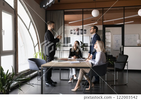 Serious team leader talking to colleagues gathered in boardroom Serious team leader talking to colleagues gathered in boardroom 122003542