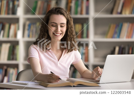 Smiling teen female study online in library using books notebook Smiling teen female study online in library using books notebook 122003548