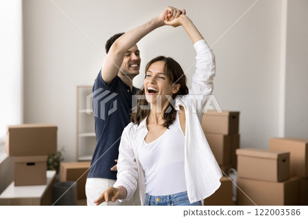 Overjoyed millennial 30s couple dancing in living room celebrate relocation 122003586