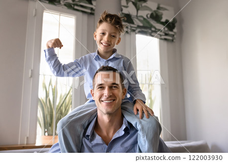 Happy kid riding fathers shoulders, showing power gesture 122003930