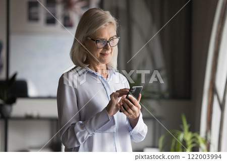 Serious middle-aged businesslady using online app on smartphone 122003994