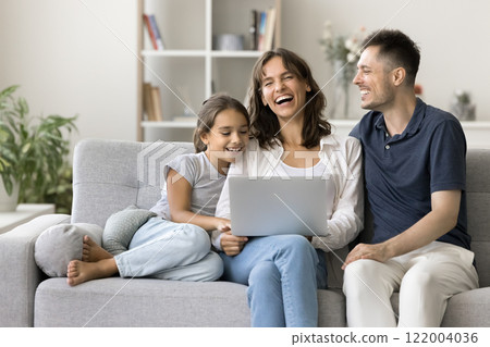 Young laughing parents with daughter watching comedy movie using laptop 122004036