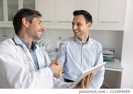 Cheerful Latin patient giving handshake to doctor with gratitude Cheerful Latin patient giving handshake to doctor with gratitude 122004089