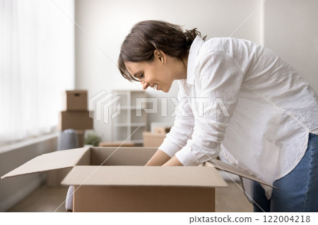 Young woman unpacking her belongings stacked in boxes 122004218