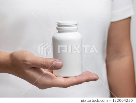 Woman in white t-shirt holding in hand a white plastic medical pill bottle closeup 122004230