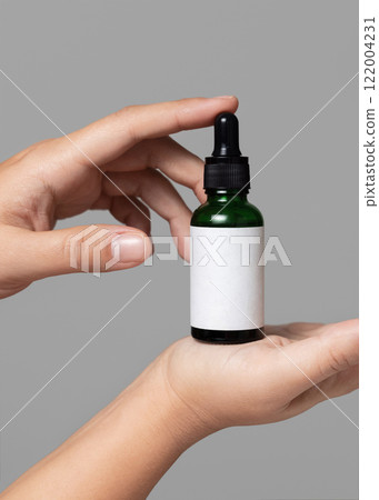 Hands holding dropper bottle with blank label against grey close up, cosmetic mockup Hands holding dropper bottle with blank label against grey close up, cosmetic mockup 122004231