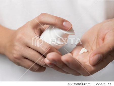 Woman squeezing hand cream on her finger and holding a cosmetic bottle in other hand, closeup 122004233
