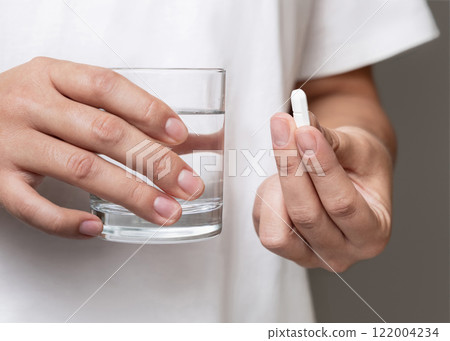 Woman in white t-shirt holding white pill in fingers and water glass in hand closeup Woman in white t-shirt holding white pill in fingers and water glass in hand closeup 122004234